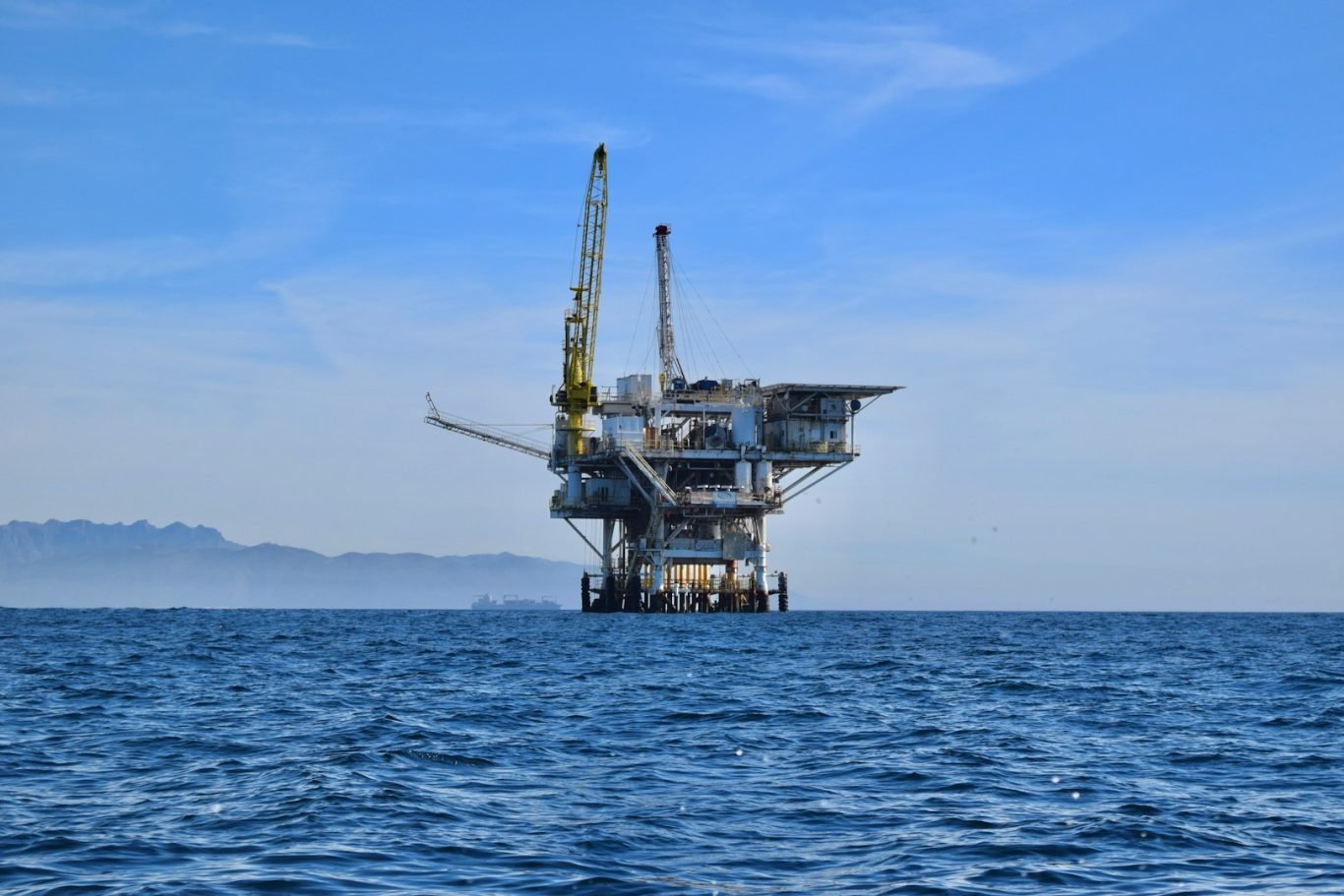 Oil & Gas Offshore oil rig with cranes in a blue sky over calm sea waters.