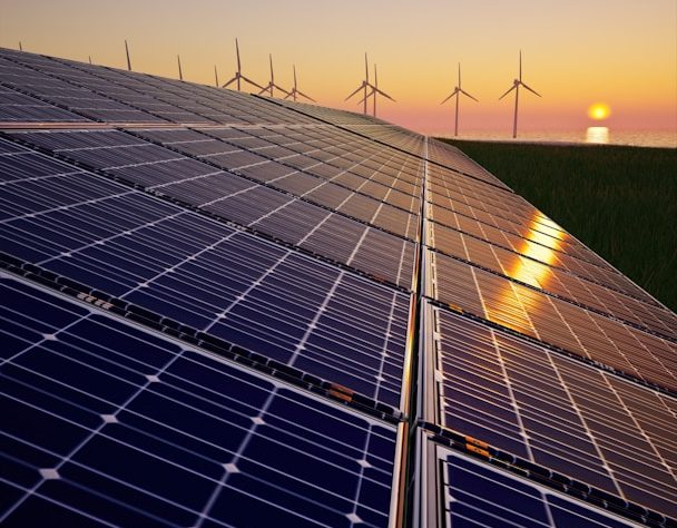 Solar panels in the foreground, wind turbines in the background, at sunset.