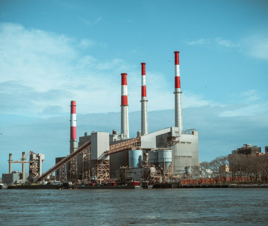 Infrastructure Industrial power plant with tall red and white smokestacks by a river under a blue sky.