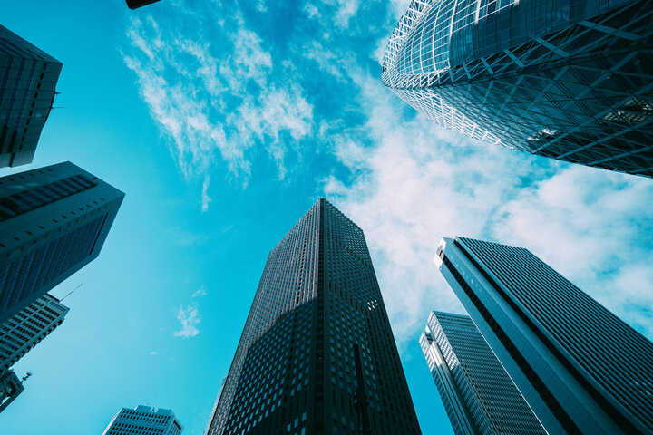 Private and Public Sectors View of skyscrapers reaching towards a bright blue sky with scattered clouds.